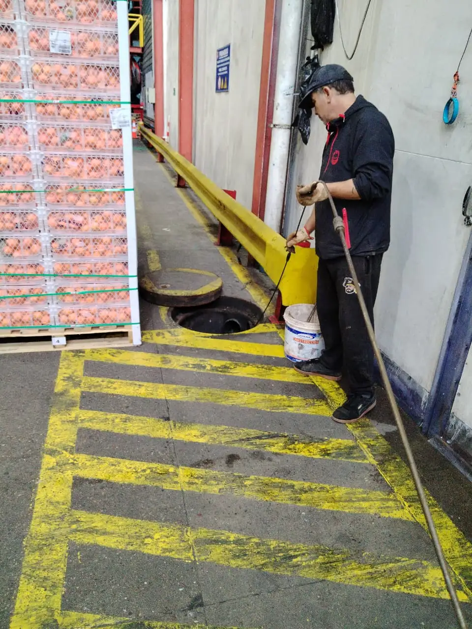 Técnico de Destapes Bravo destapando con varilla la cámara de una bodega industrial, junto a pallets de mercadería